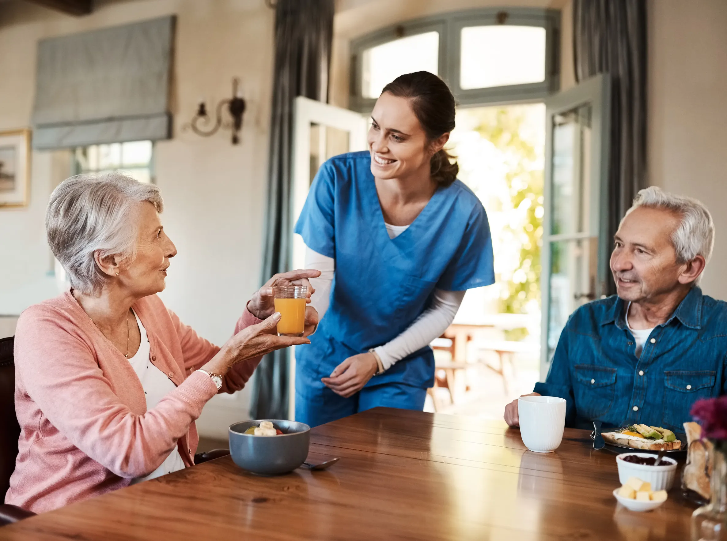 Happy, talking and caregiver with elderly patients for fruit drink in retirement home